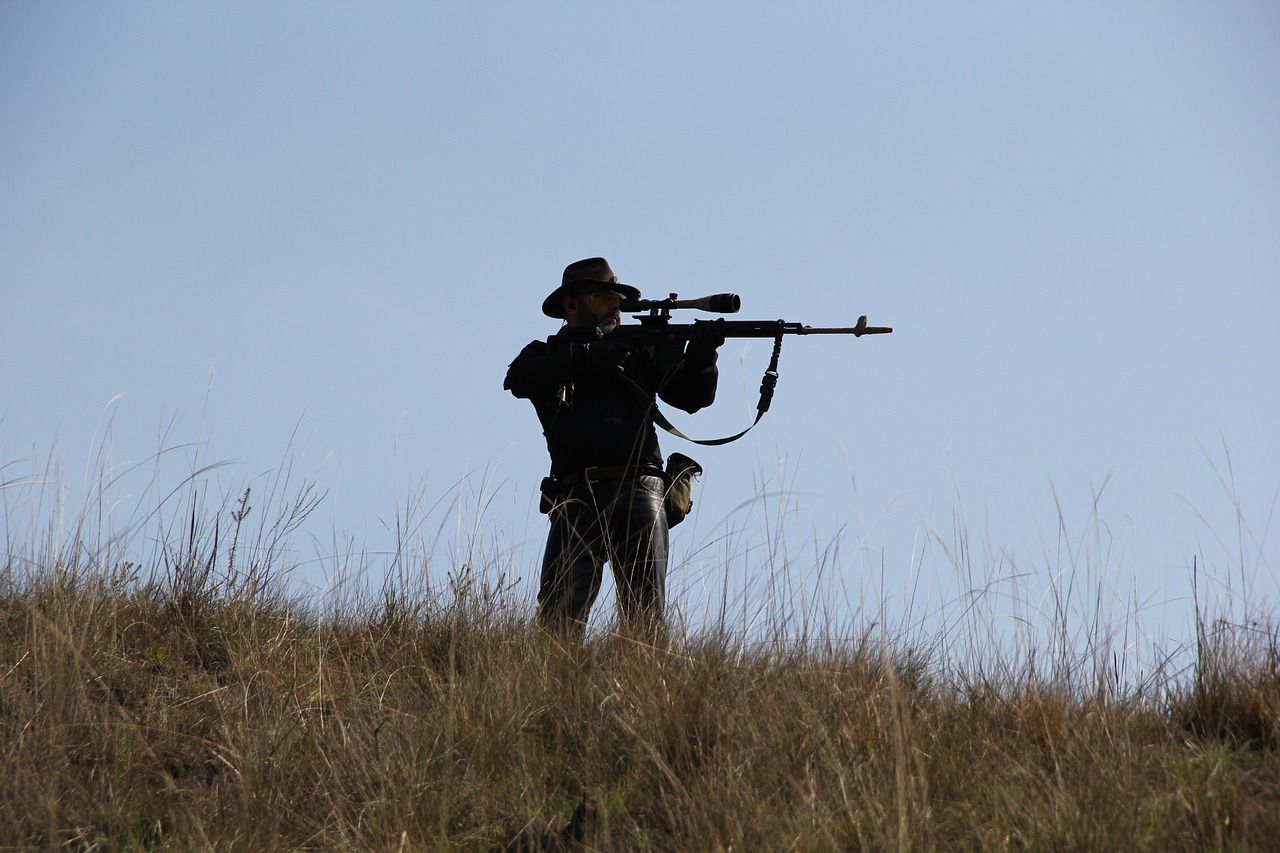 a man standing on a hill while holding up this gun and aiming at his target