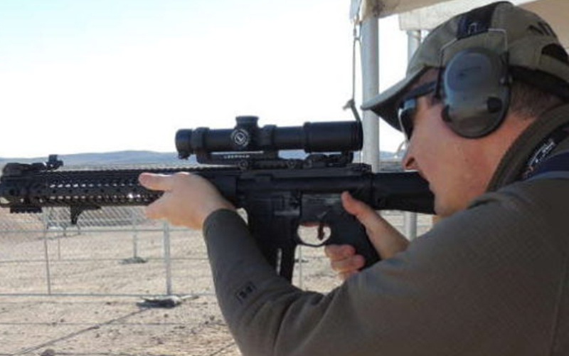 a man in target shooting practice, holding up a rifle and looking through the attached 1-4x scope