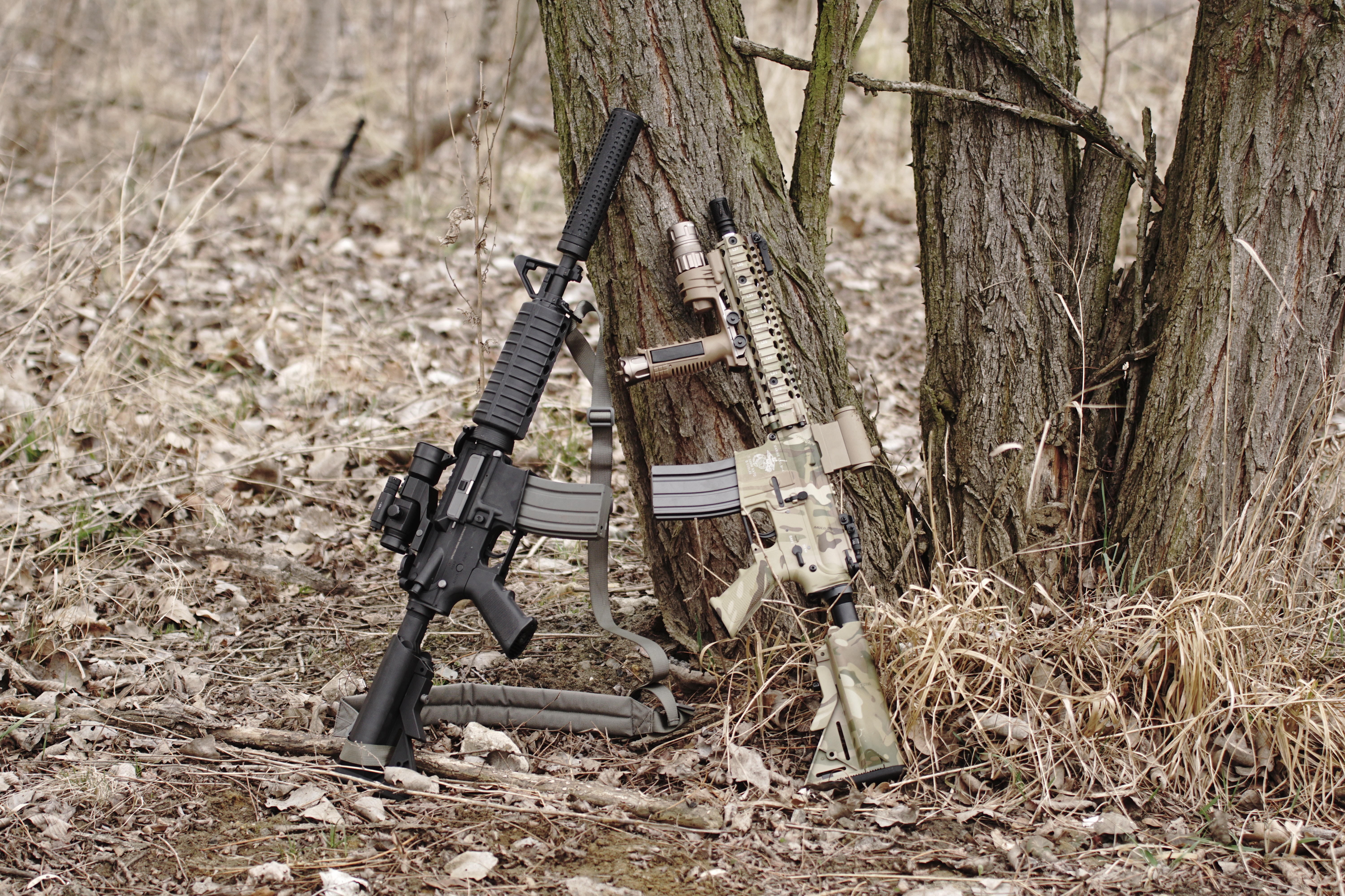 two rifles with scopes vertically leaning on a tree trunk