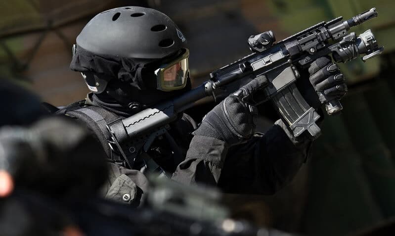 man in combat uniform holding a rifle and looking through the scope