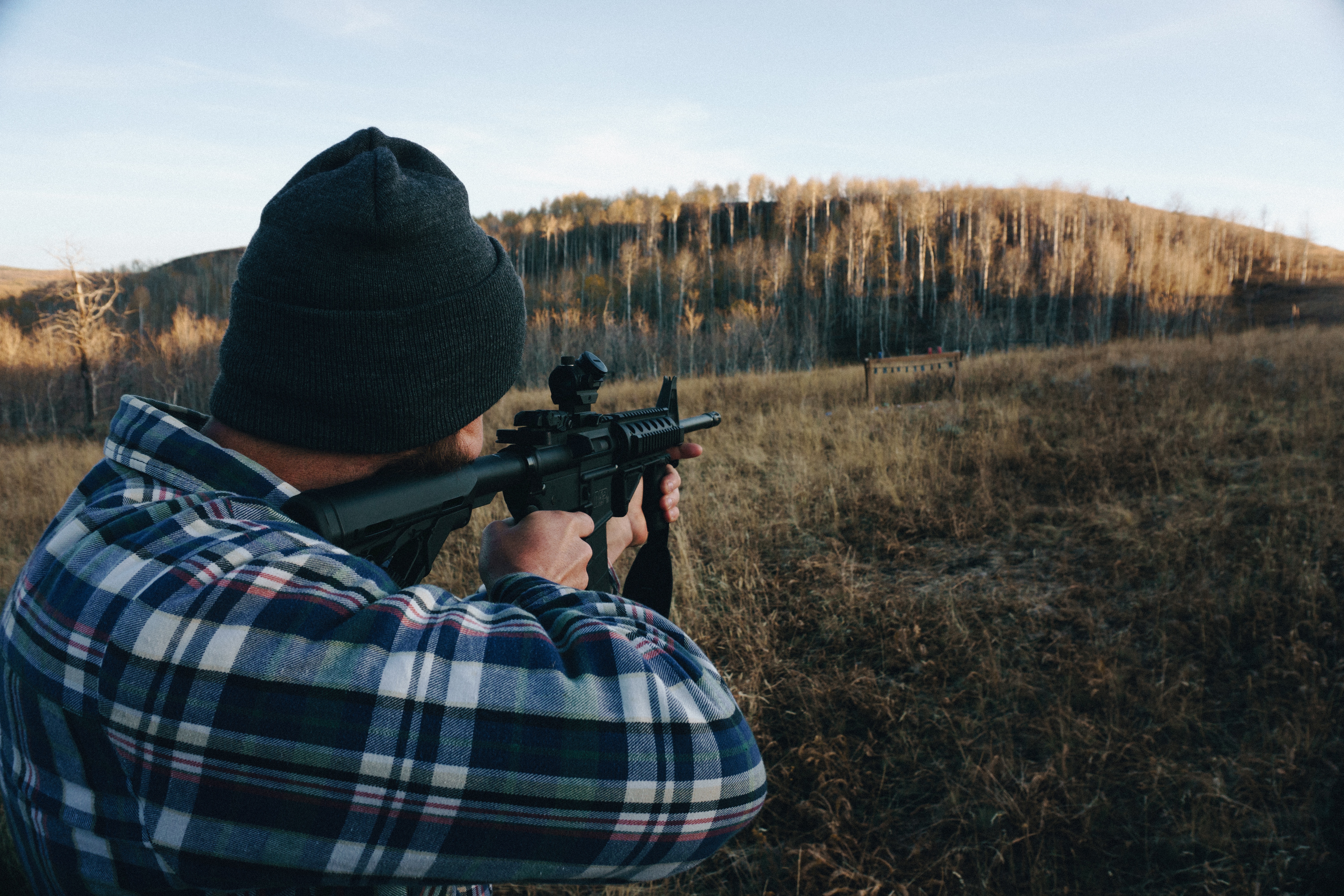 a hunter looking through the rifle scope attached to the firearm he is holding